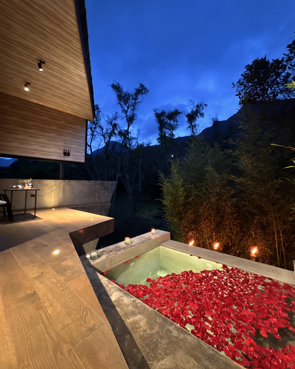 Jacuzzi privado cubierto de pétalos de rosa con velas y antorchas al anochecer