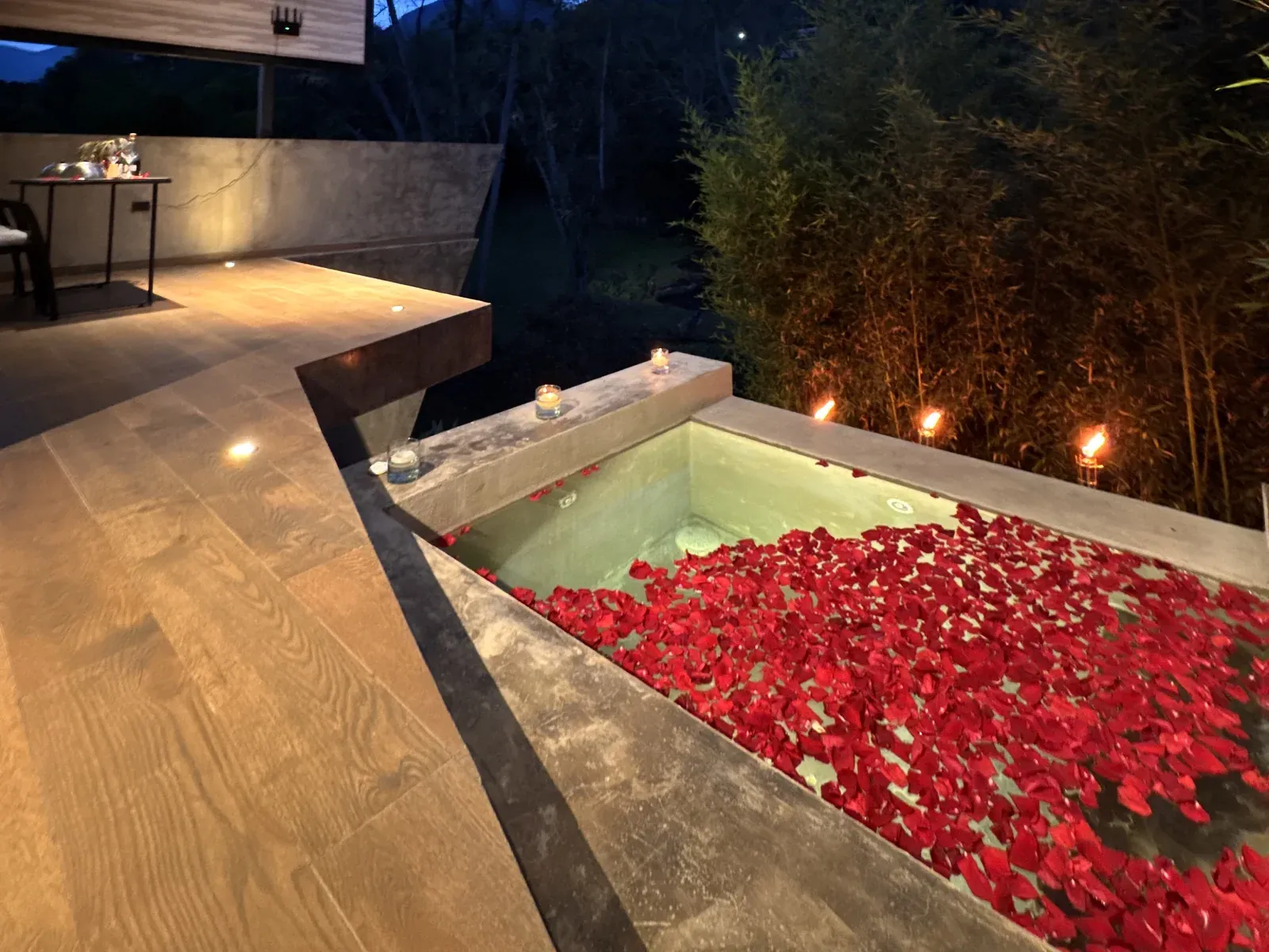 Jacuzzi privado cubierto de pétalos de rosa, con velas y antorchas al anochecer